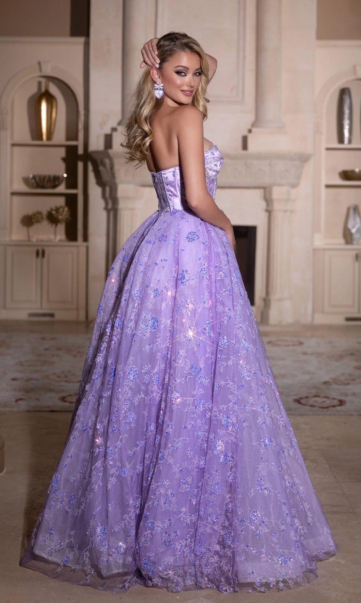 A woman poses indoors in the Portia and Scarlett PS25315 long prom dress, featuring a strapless, sweetheart neckline with floral embellishments, sparkling details, and matching earrings.